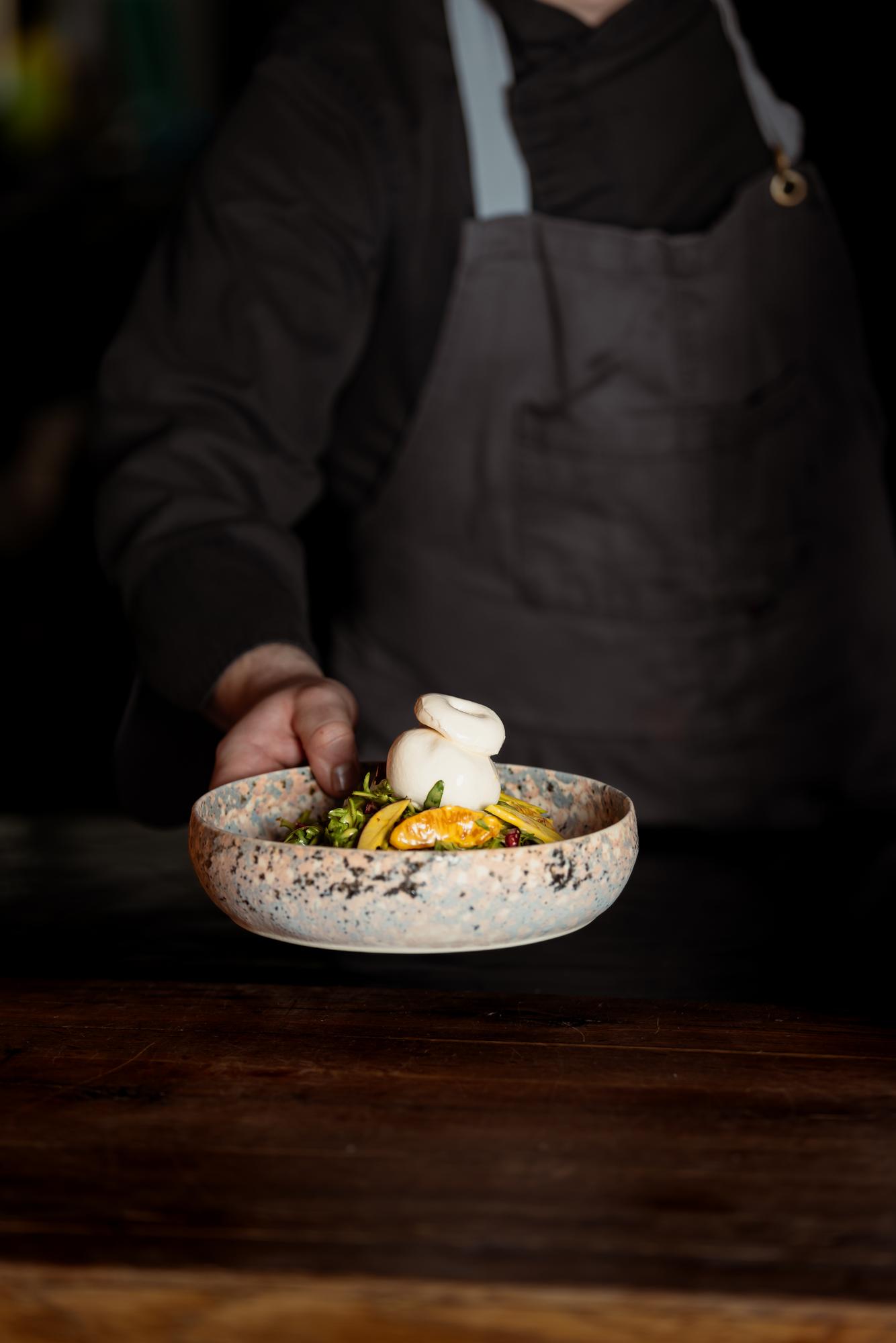 Chef presenting plated dish on dark table